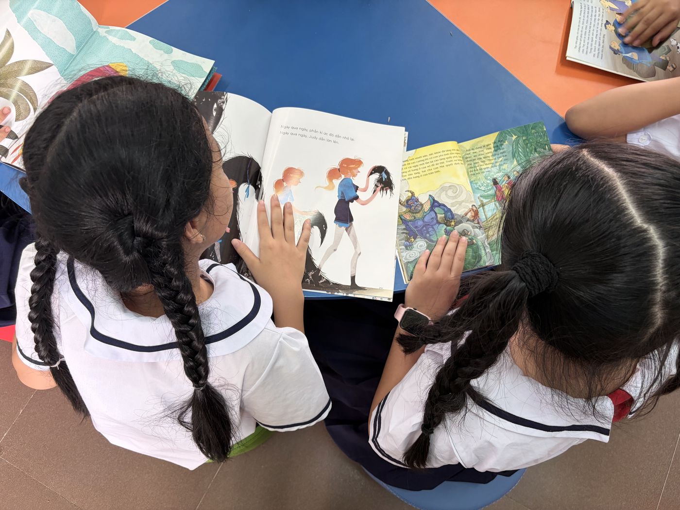 Two schoolgirls sharing a picture book on the floor of a creative library